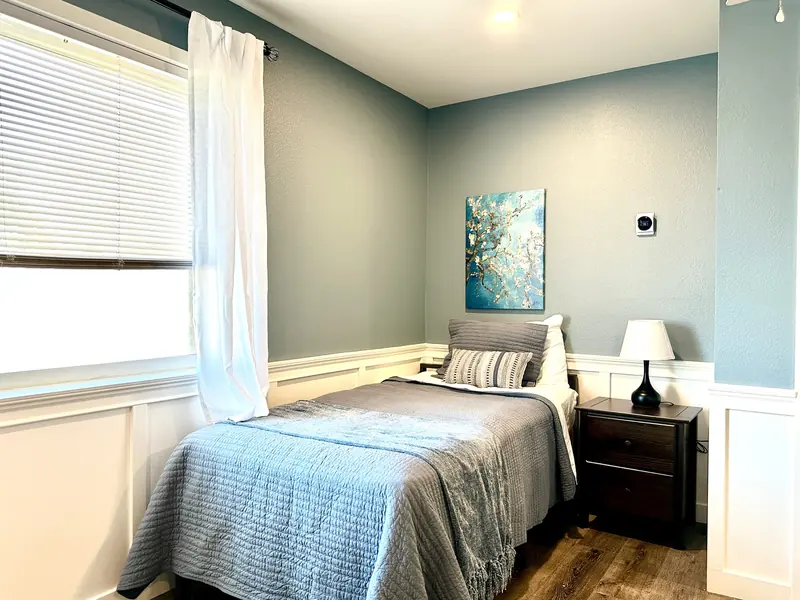 Bed by a bright window with sheer curtains