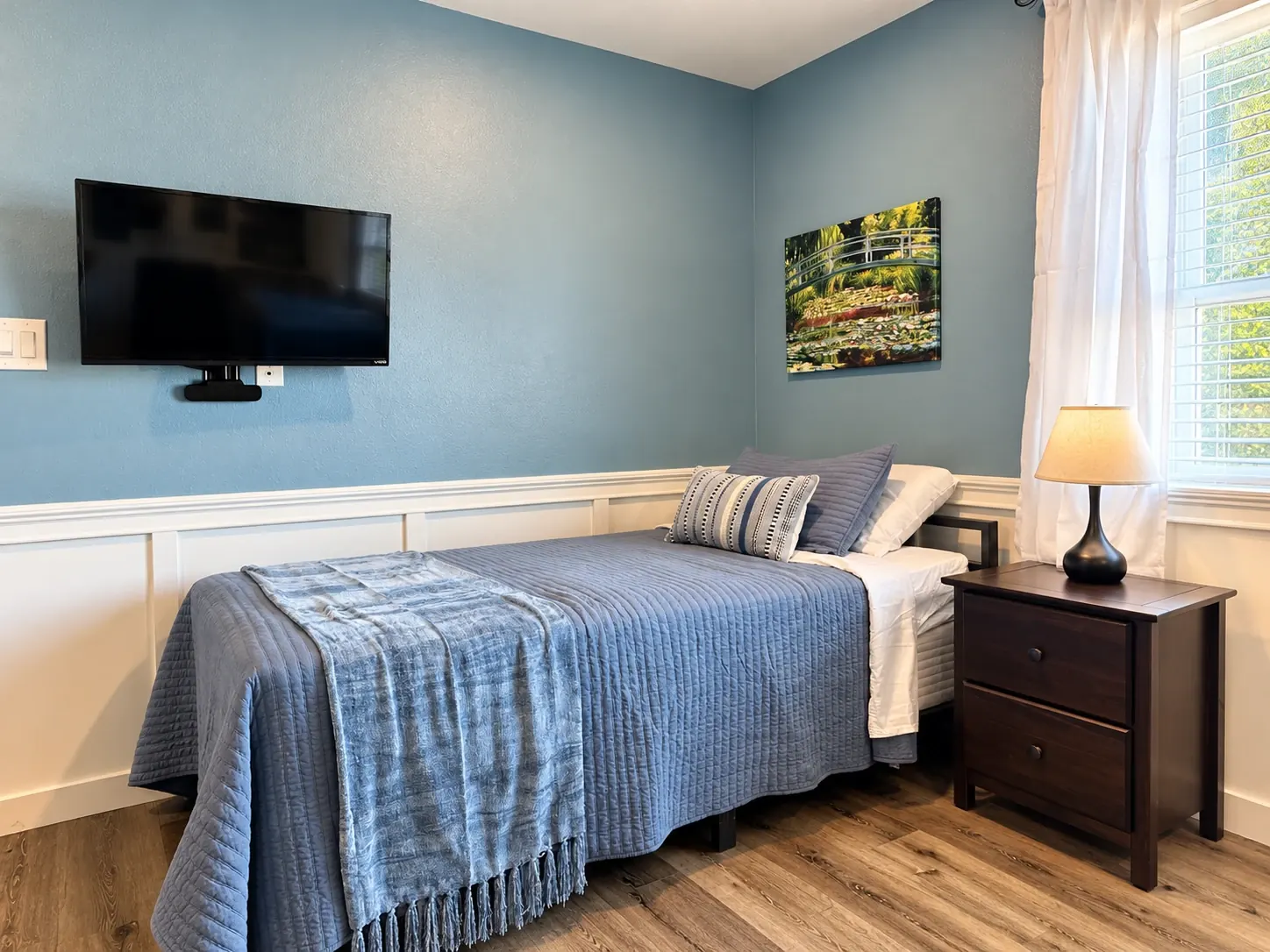 Bed with blue quilt, nightstand, lamp and TV