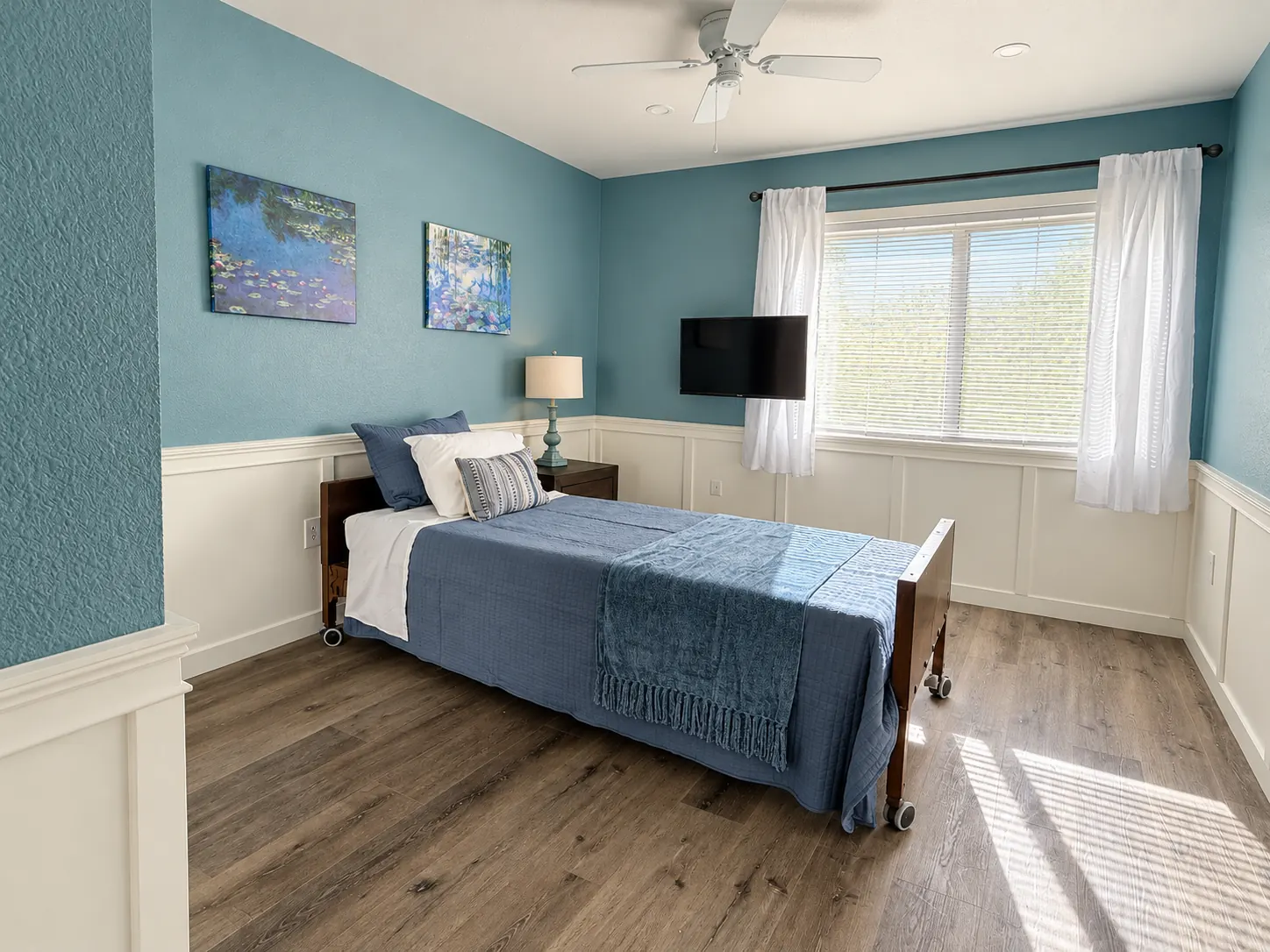 Sunlit renovated room with soft blue walls, white wainscoting and wood floors